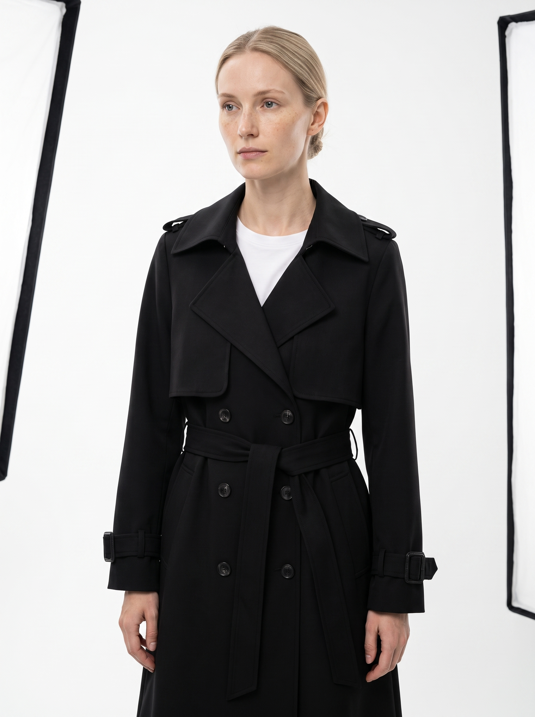 Kvinde i en sort dobbeltradet trenchcoat til dame fotograferet i studie mod hvid baggrund — Bjerrelund